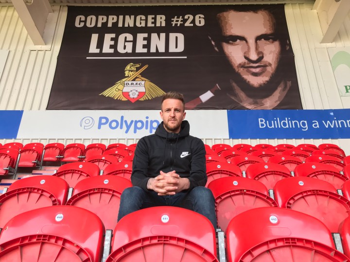 James Coppinger sits in the seats at Doncaster Rovers Keepmoat Stadium in front of a banner celebrating him