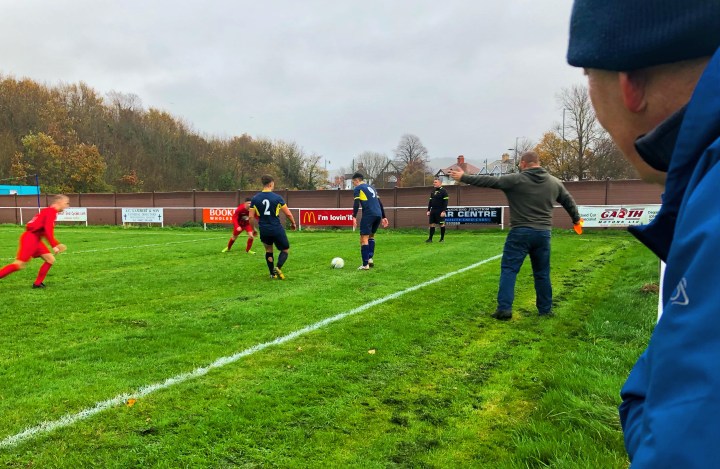 An assistant referee gestures at players from Llandudno Junction and Penmaenmawr Phoenix during a match