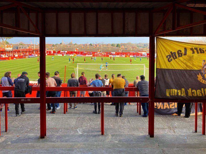 The view of the match from the back of the covered terrace at Alfreton Town's ground is partially obscured by a big yellow and black flag belonging to the visitors Southport