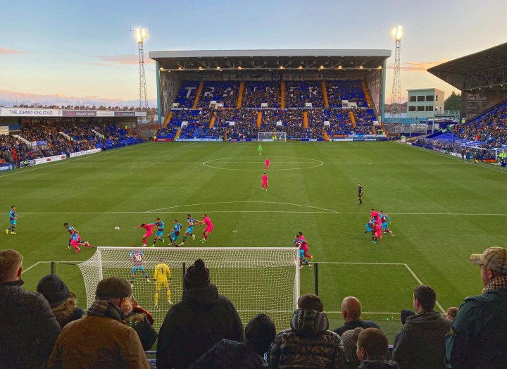 The silhouettes of fans seen from behind as they watch Tranmere Rovers in claret and blue take on Doncaster Rovers in pink at Prenton Park on Boxing Day 2022