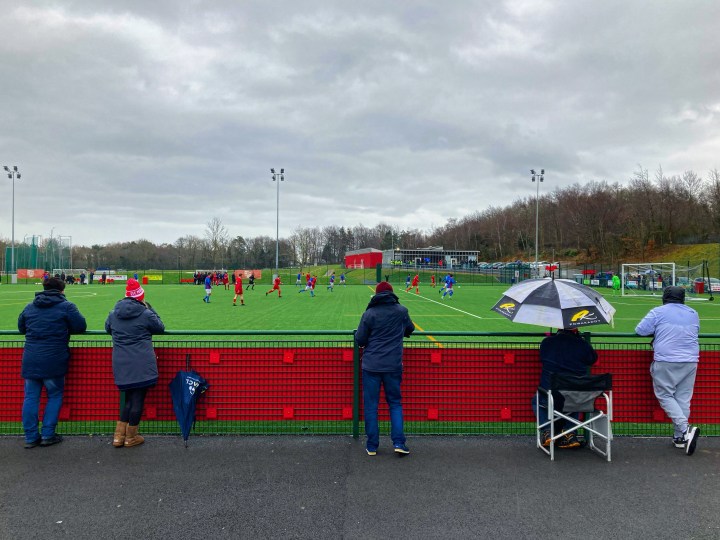 Five fans including one under an umbrella watch from te touchline as Bangor 1876 play Denbigh Town