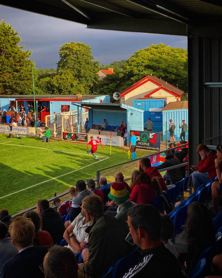 Colwyn Bay's number 10 takes a corner kick as his team's fans watch on during a Cymru Premier match against Caernarfon Town at Llanelian Road