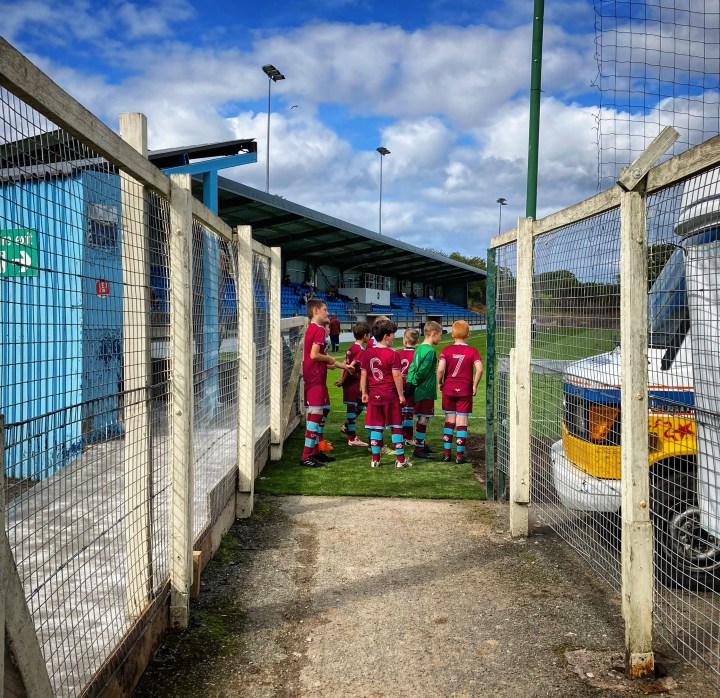 A group of young Colwyn Bay mascots stand in the tunnel looking out onto the pitch at Bay's Llanelian Road ground