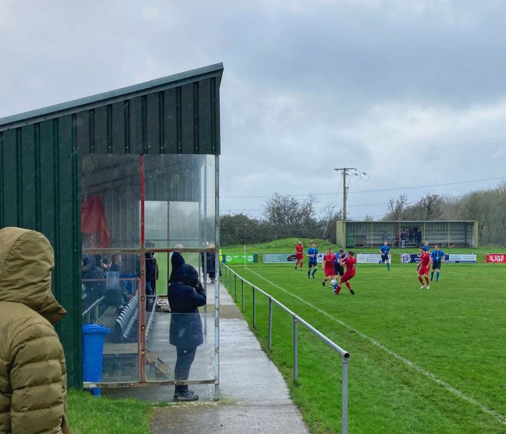 Players from Llanfairpwl and Trethomas Bluebirds challenge for the ball in the rain in front of the stands at the former's home
