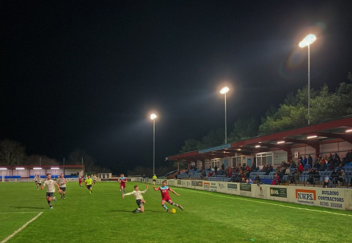 A Pontypridd player slides in to challenge a Colwyn Bay player during their match under the floodlights at Llanelian Road