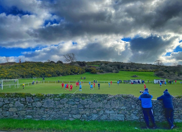 Two Pentraeth supporters, one with a camera, watch over a stone wall as their team takes on Glantraeth