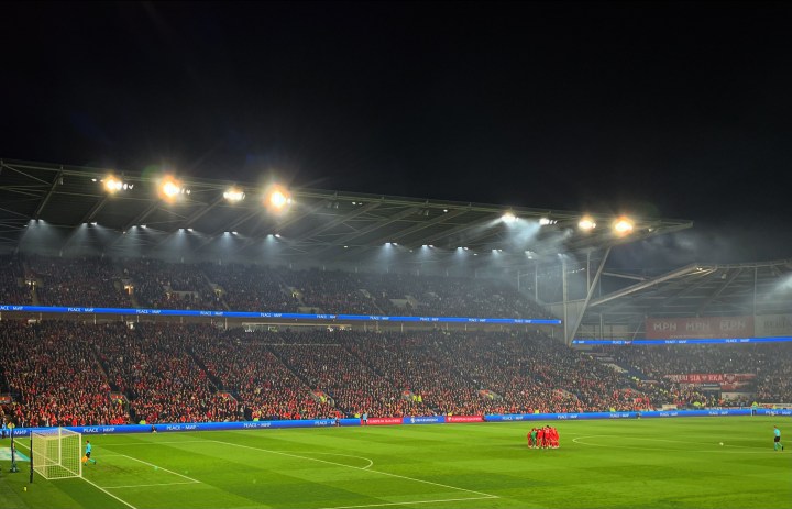 Wales players have a pre-match huddle in front of the full stands at Cardiff City Stadium as they prepare to take on Poland under floodlights