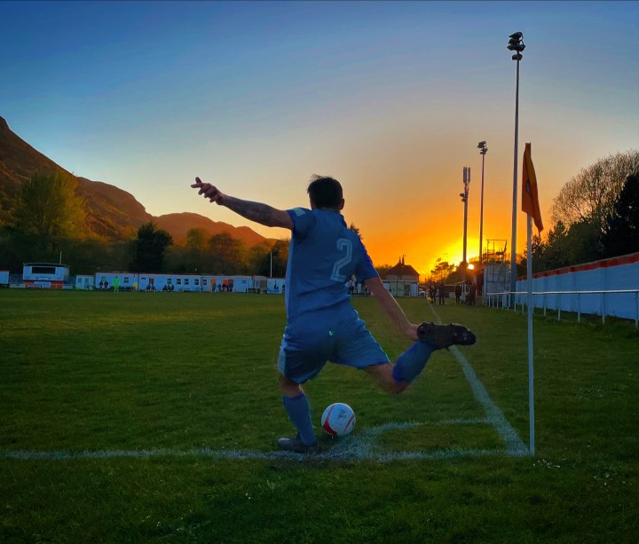 A Holyhead Hotspur player is silhouetted by the setting sun as he takes a corner at Conwy Borough's Y Morfa