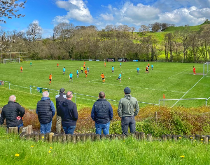 A small group of supporters watch on from a grass bank as Llansannan play NFA at the former's Llan Siro ground, surrounded by trees and green hills