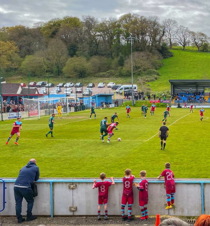 Young kids in full kit watch on over the pitchside fence as Colwyn Bay play Barry Town United at Bay's Llanelian Road ground