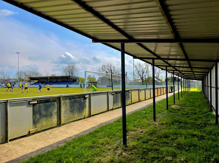 A Llangefni Town player shoots for goal, as seen from the empty covered stand behind the goal at Cae Bob Parry during Llangefni's home defeat to Hawarden Rangers