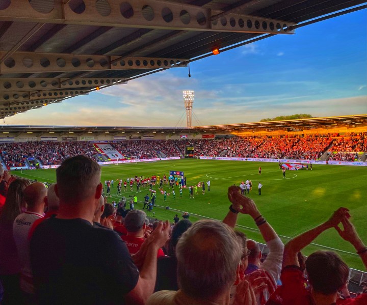A packed Eco-Power stadium welcomes the players out onto the field for Doncaster Rovers home play-off semi-final against Crewe Alexandra, the setting sun highlighting the fans in the East Stand