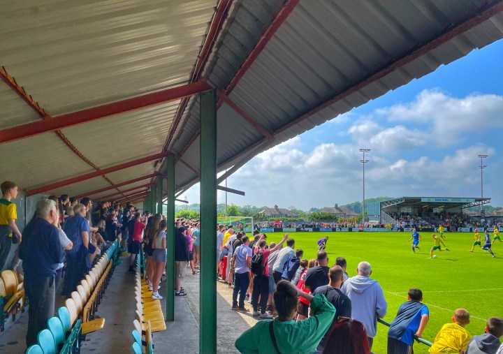 Sion Bradley of Caernarfon Town scores his team's third goal in their European play-off win over Penybont at The Oval, as the home fans watch on behind the goal