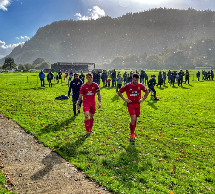 Llanrwst United players leave the field at half time as rain starts to fall despite the bright sunlight