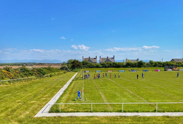 Bethesda Athletic take a corner away at Aberffraw; dry fields and the outline of the mountains of Eryri are visible beyond the pitch