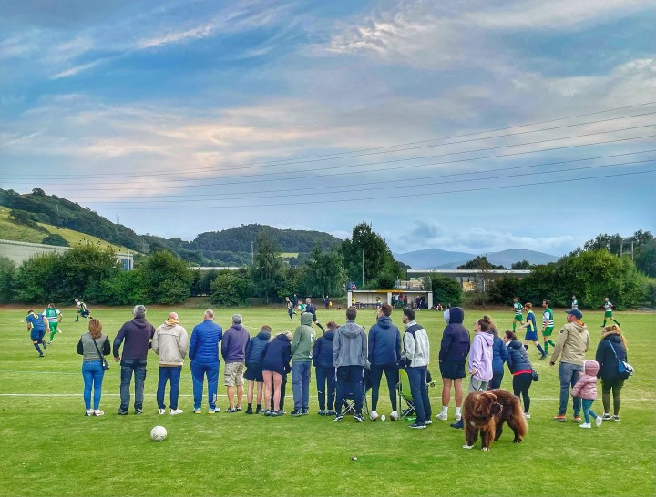 A line of spectators, and a giant dog, watch Mochdre Sports go on the attack against Llandudno Amateurs