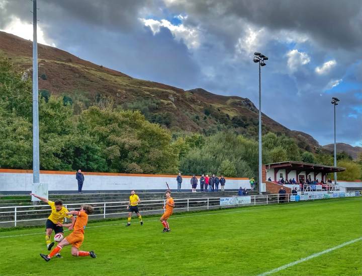 A Conwy defender tackles a Porthmadog winger as a handful of spectators watch on from the terrace