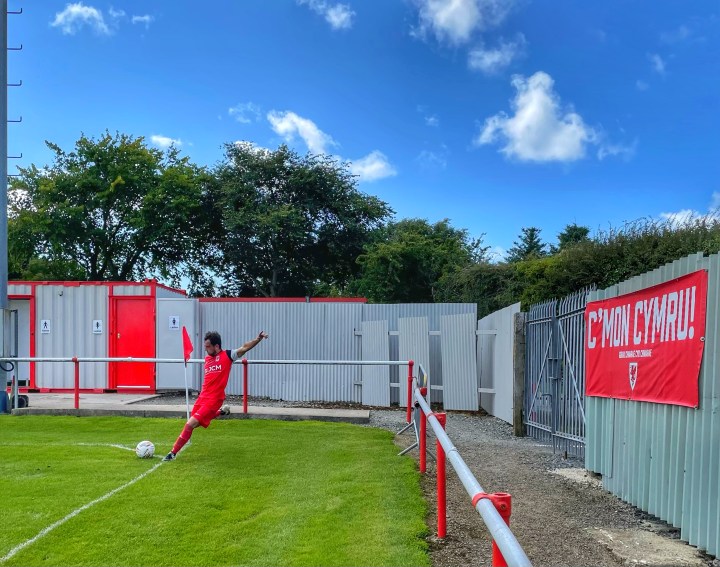 A Cemaes Bay player takes a cornerin front of a large 'C'mon Cymru' banner