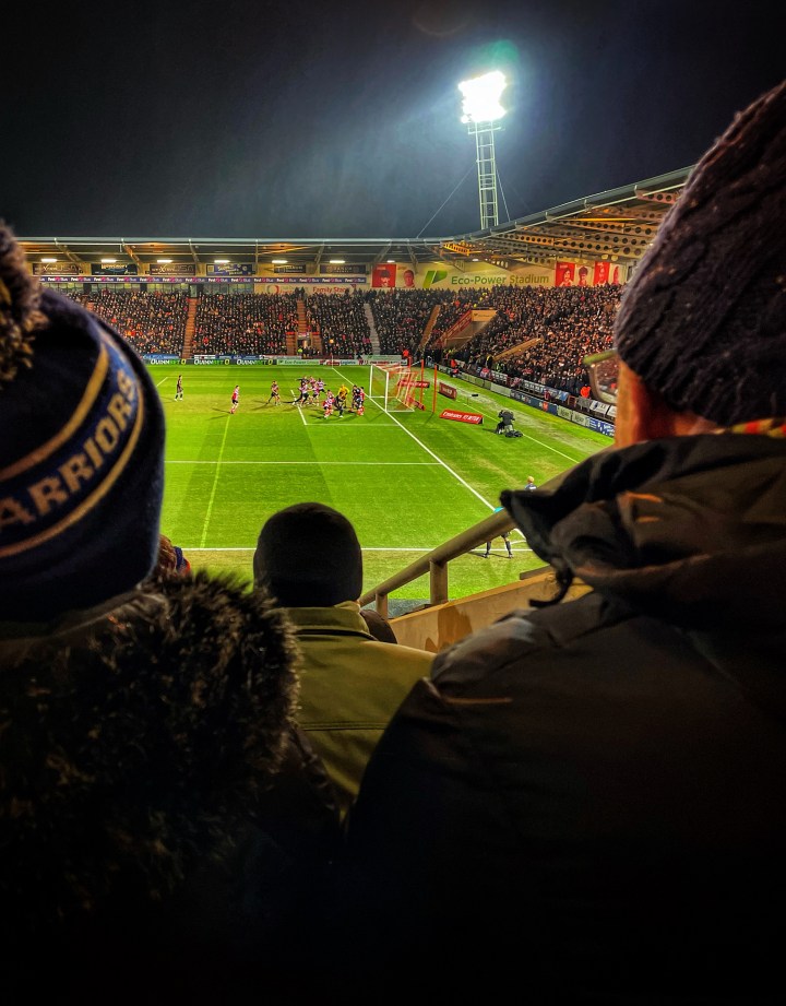 Goalmouth action at the Eco Power Stadium viewed between fans in the stands wrapped up against the cold