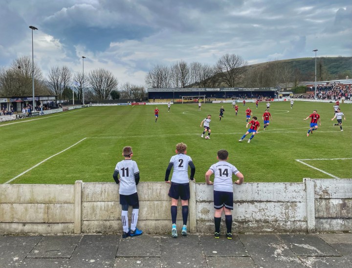 Three young Mossley fans watch on as their team attack at home to Whythenshawe