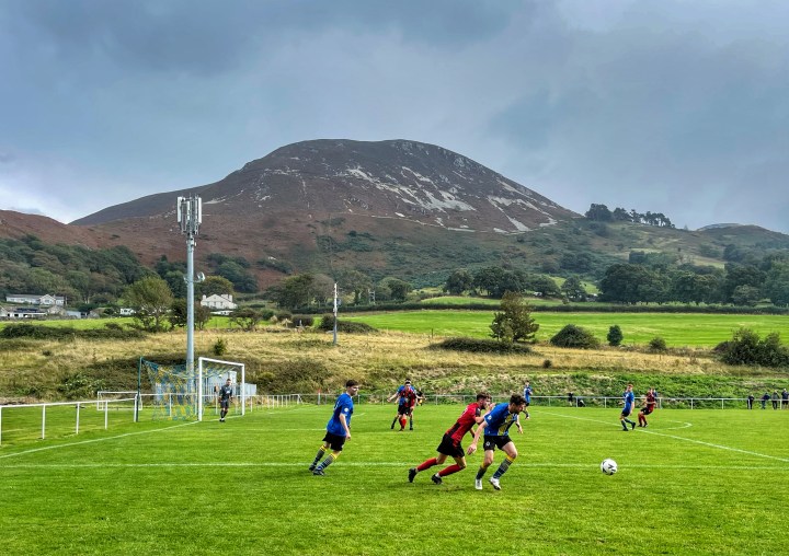 Players challenge for the ball in front of a mountainous backdrop