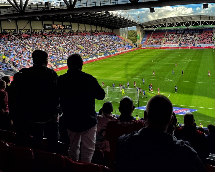 Doncaster Rovers fans high in the stand are silhouetted by the sunshine during a defeat at Wigan