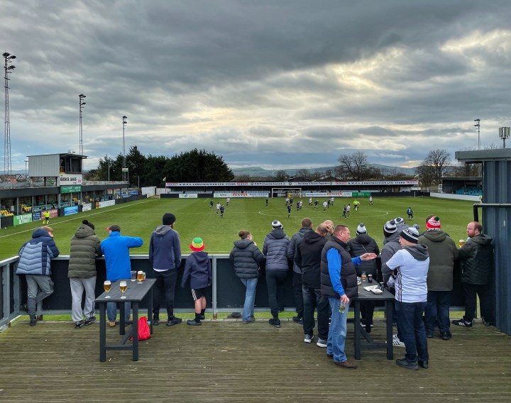 Rhyl supporters stand on the terrace beside the club bar as their team's FAW Welsh Cup tie against Cwmbran Town takes place behind them.