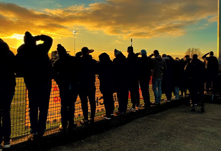 Silhouetted supporters shield their eyes and look into the setting sun during Caernarfon Town's defeat to Colwyn Bay at Llandudno.
