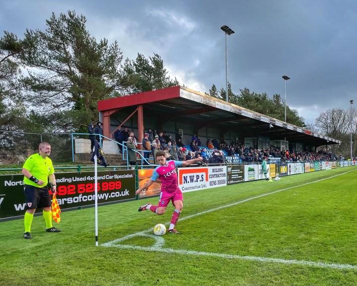 A Colwyn Bay player takes a corner in front of the home support at Llanelian Road.