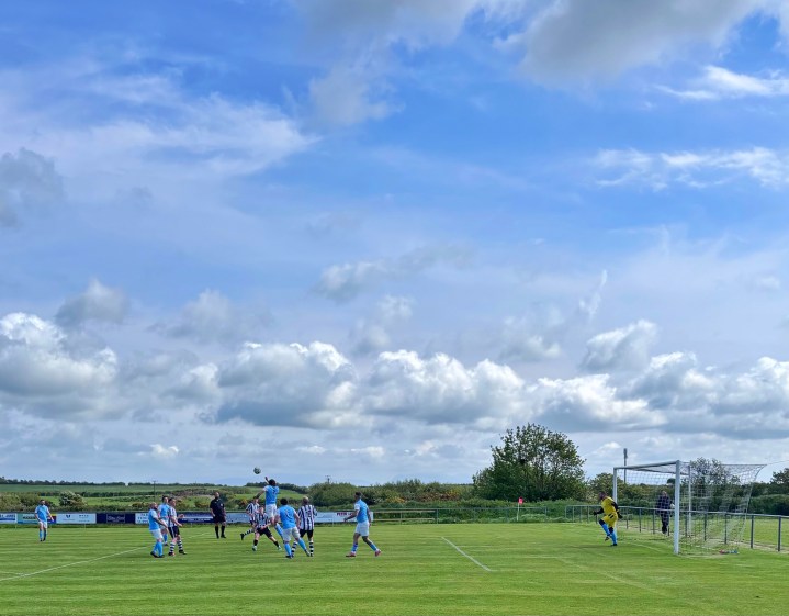 A Bontnewydd defender rises to head clear a cross beneath a huge blue Ynys Môn sky at Gwalchmai.