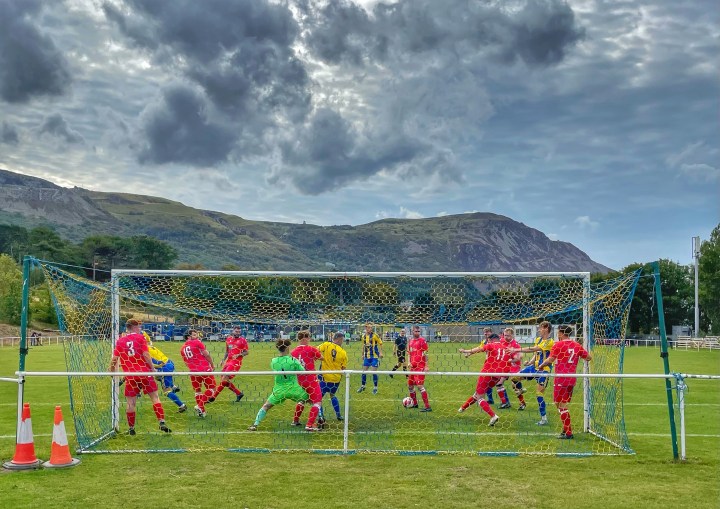 A goal mouth scramble during Penmaenmawr Phoenix vs Waterloo Rovers against a mountain backdrop.