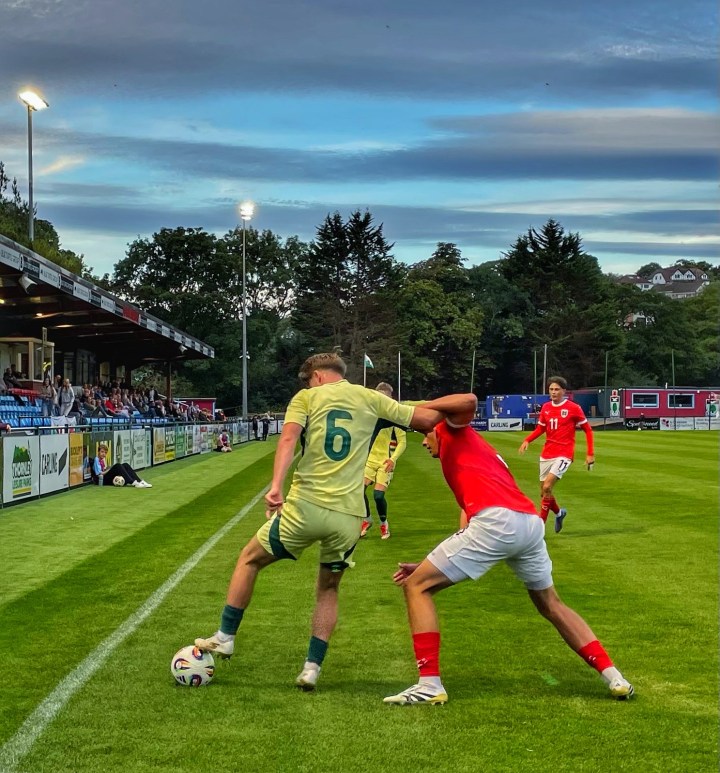 A Wales defender holds off an Austrian player by the touchline during an under 19s international at Colwyn Bay