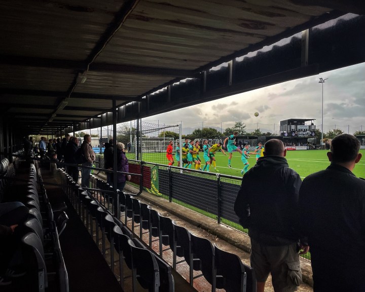 Supporters watch some goal mouth action unfold from the dry safety of the stand behind the goal during a soggy Caernarfon Town match at their temporary home in Llandudno.